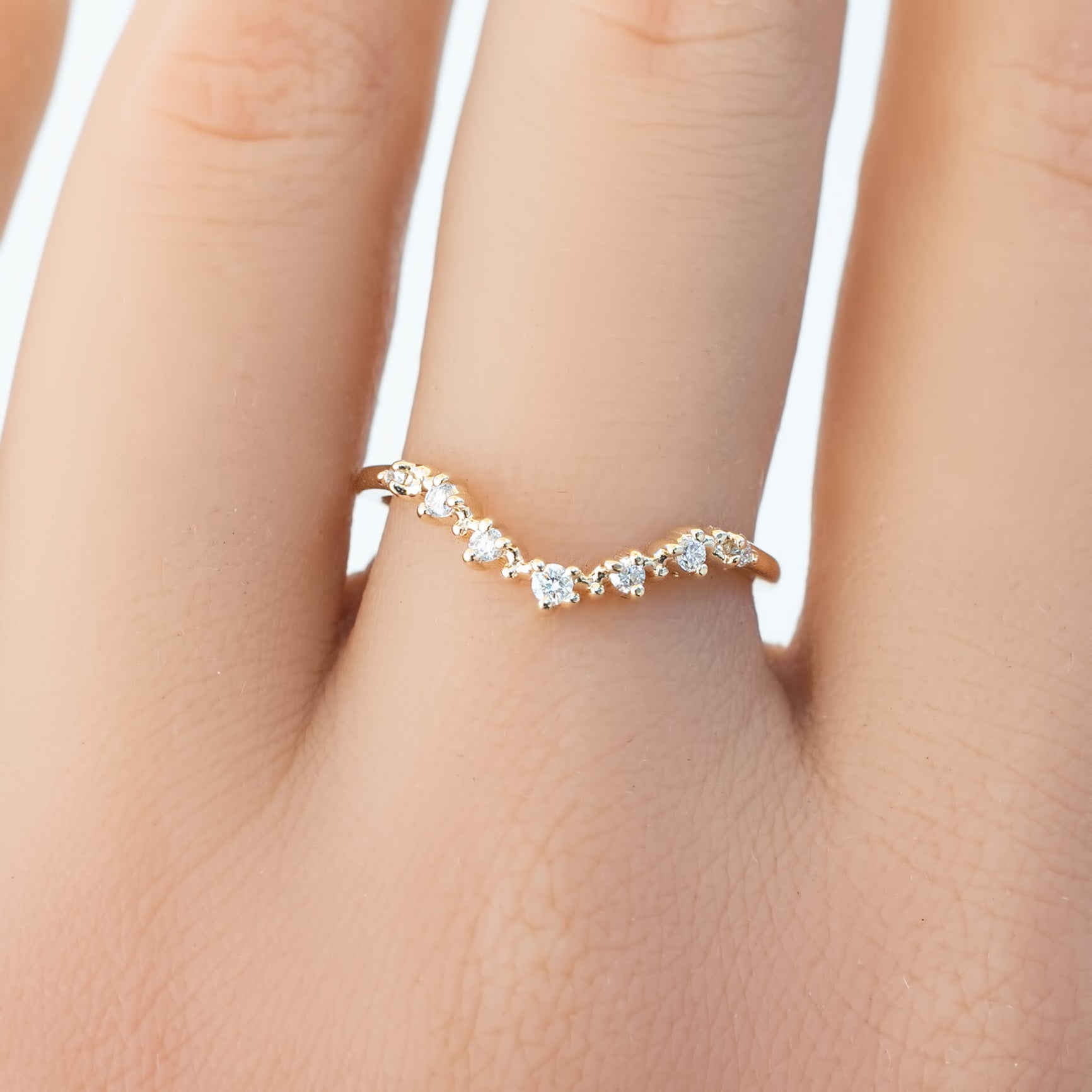 Close-up of a solid gold Norah Tiara Ring with natural white diamonds in a curved V-shape on a finger