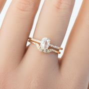 Oval white diamond ring with curved solid gold band and small accent diamonds on finger
