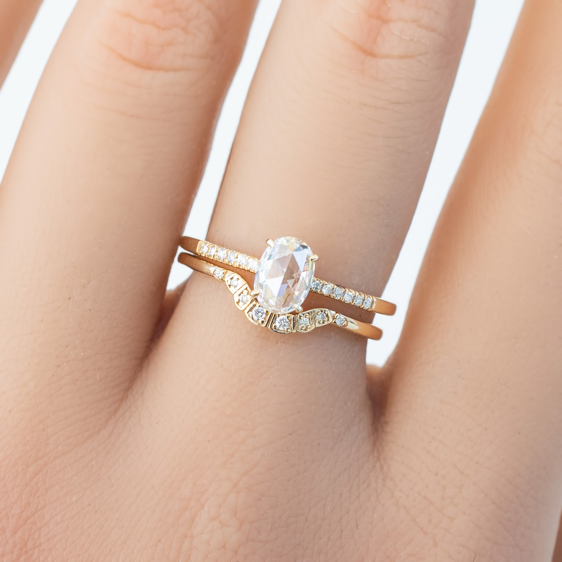 Oval white diamond ring with curved solid gold band and small accent diamonds on finger