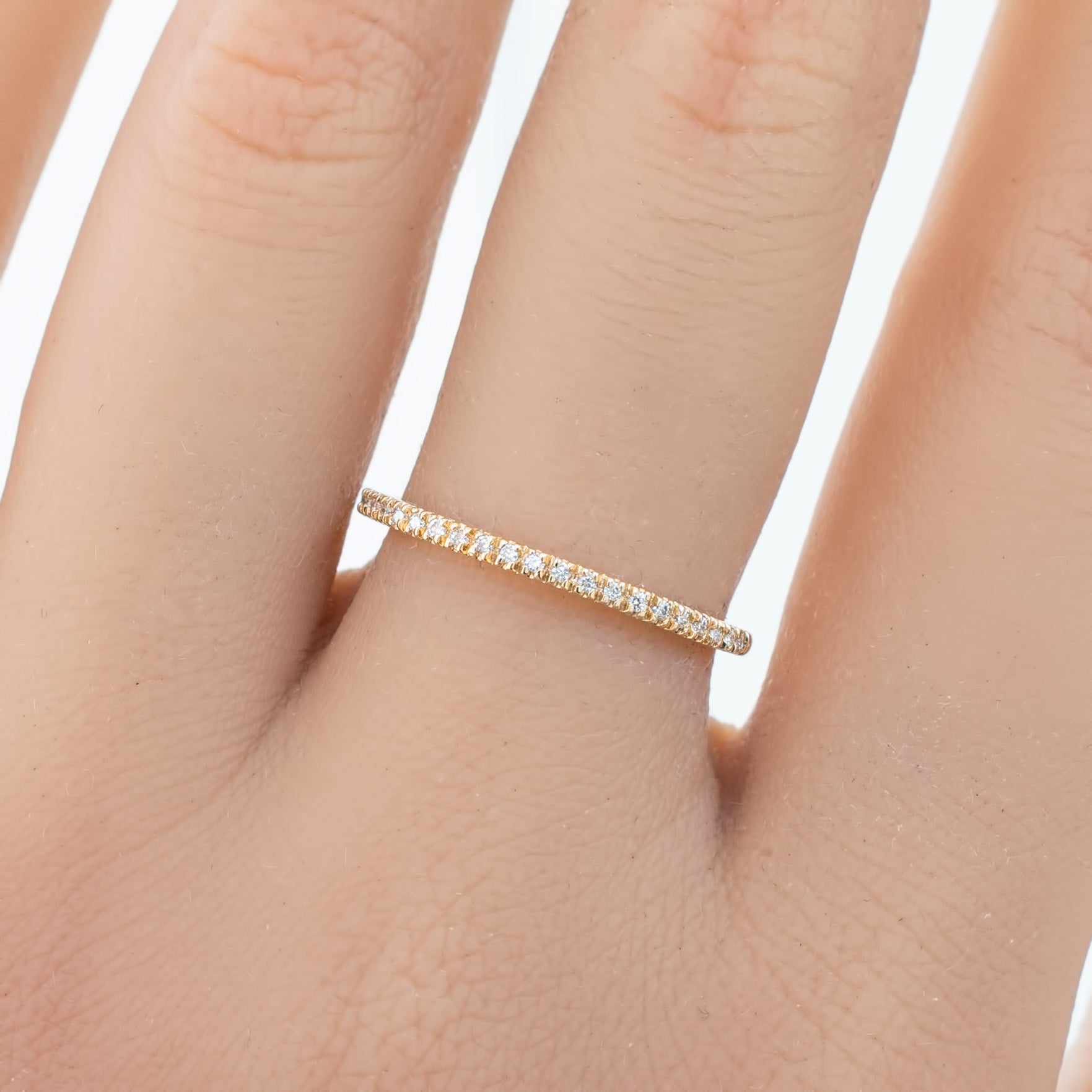 Close-up of hand wearing a delicate 1.3mm gold meteor diamond band with small white diamonds set around it
