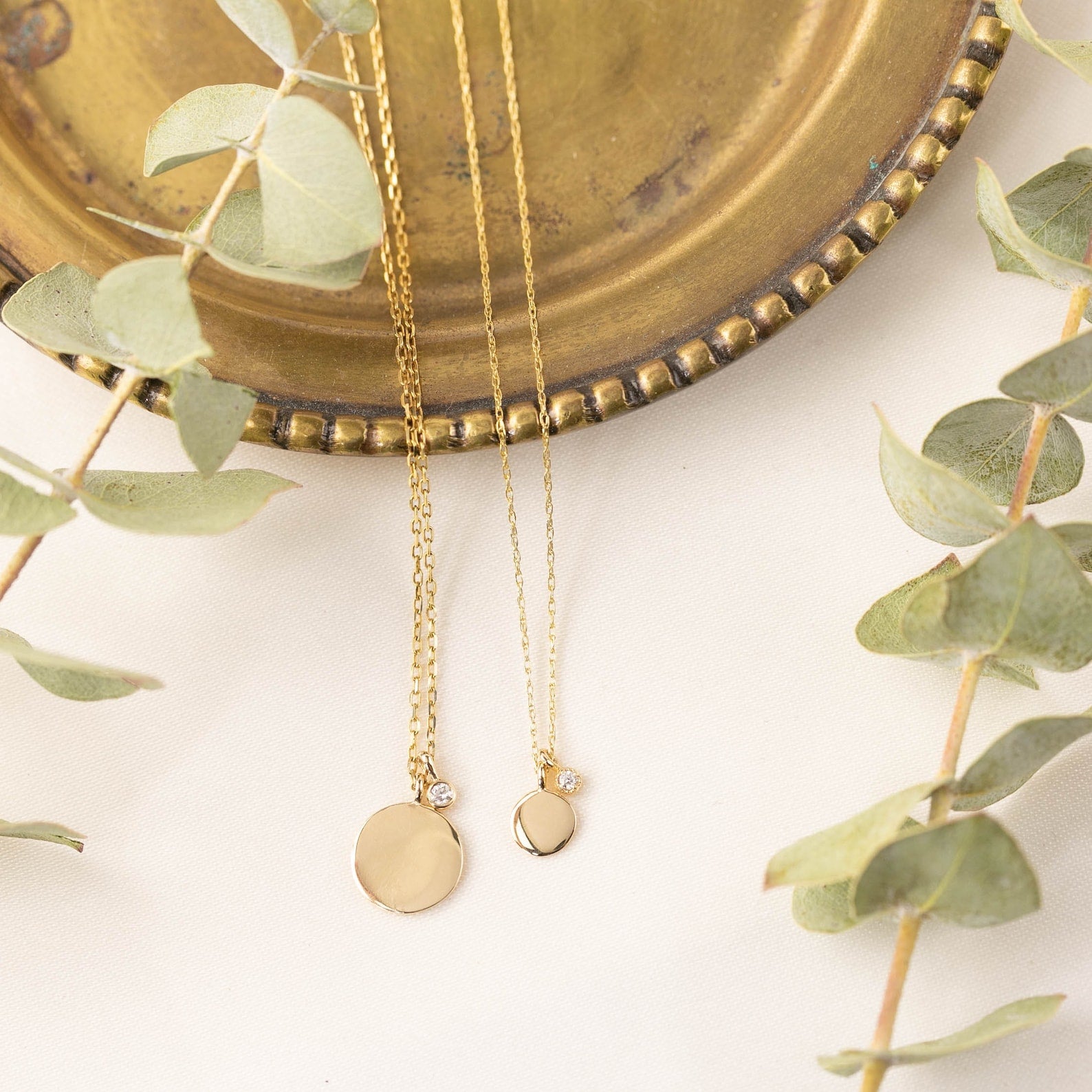 Two gold necklaces with pendants on a decorative plate with greenery