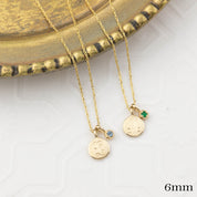 Two gold necklaces with round pendants on a white surface