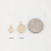 Two gold pendants with sizes 6mm and 9mm next to a quarter for scale on a white background