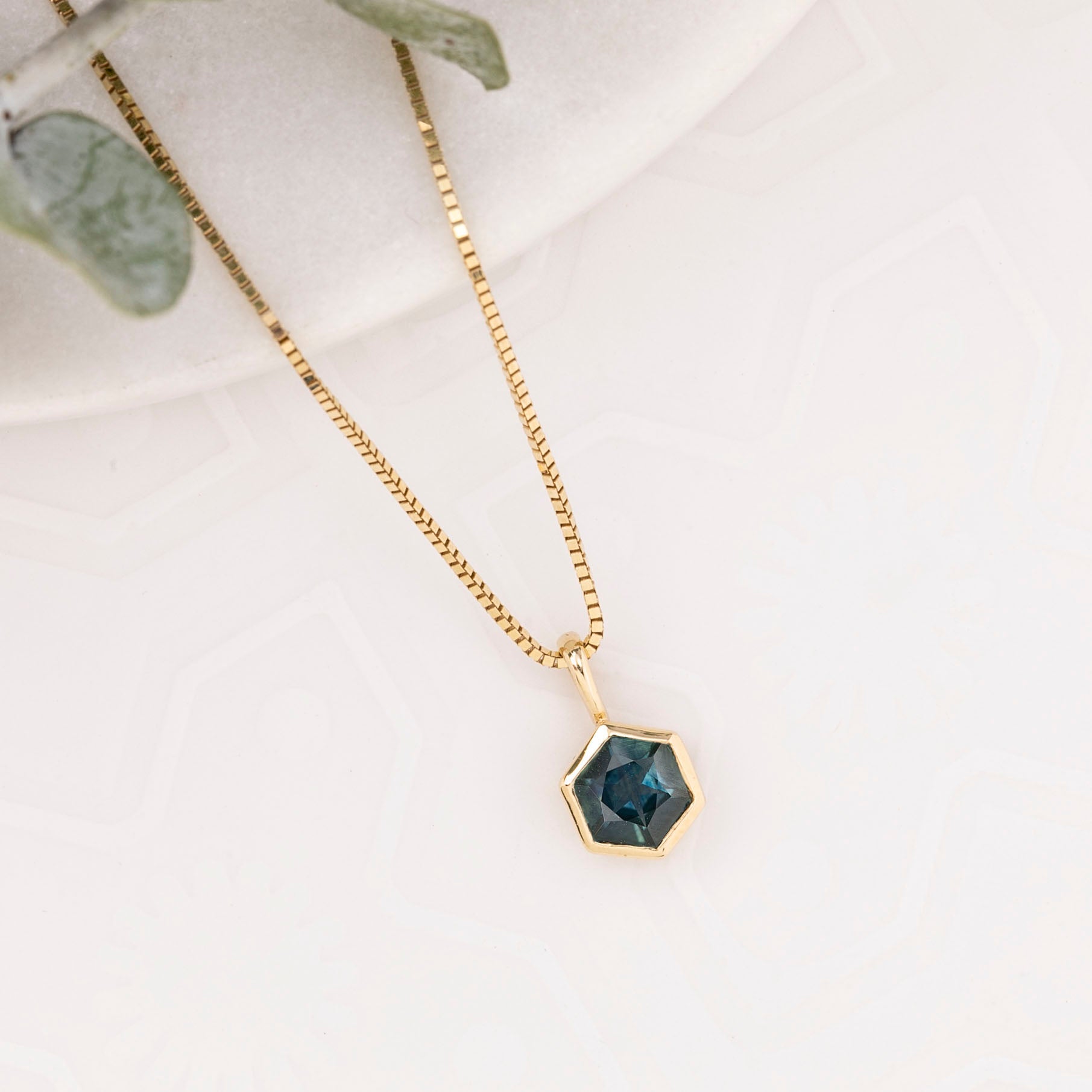 Gold necklace with a hexagonal pendant on a light background