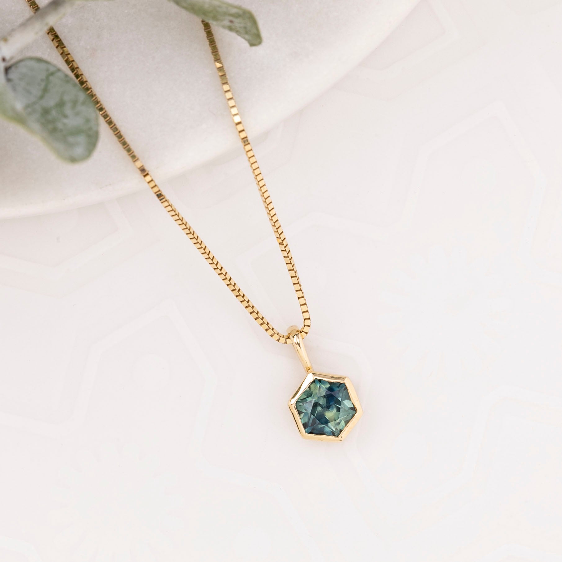 Gold necklace with a green hexagonal pendant on a light background