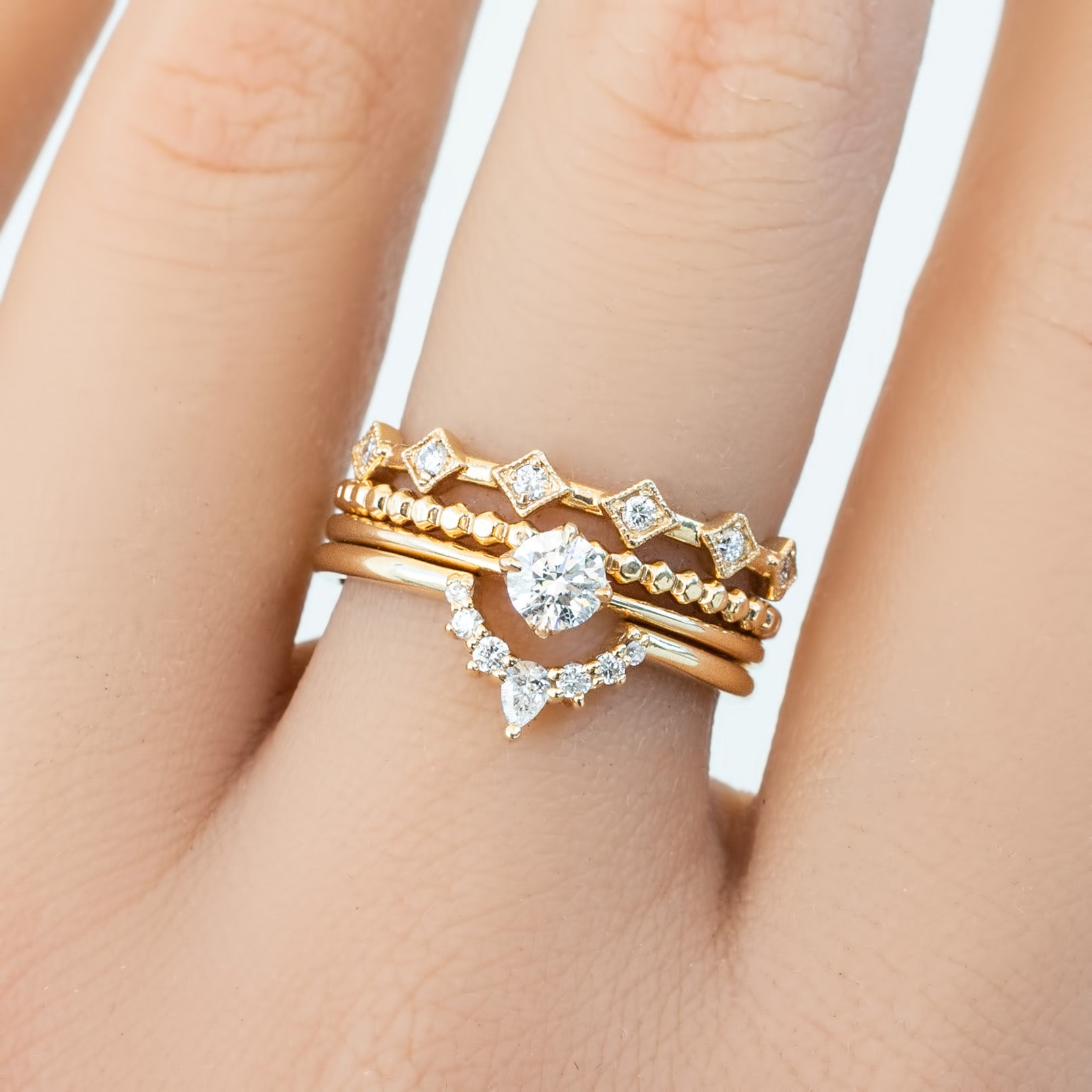 Stacked six star ring set featuring natural white diamonds in solid gold on a hand with smooth skin background.