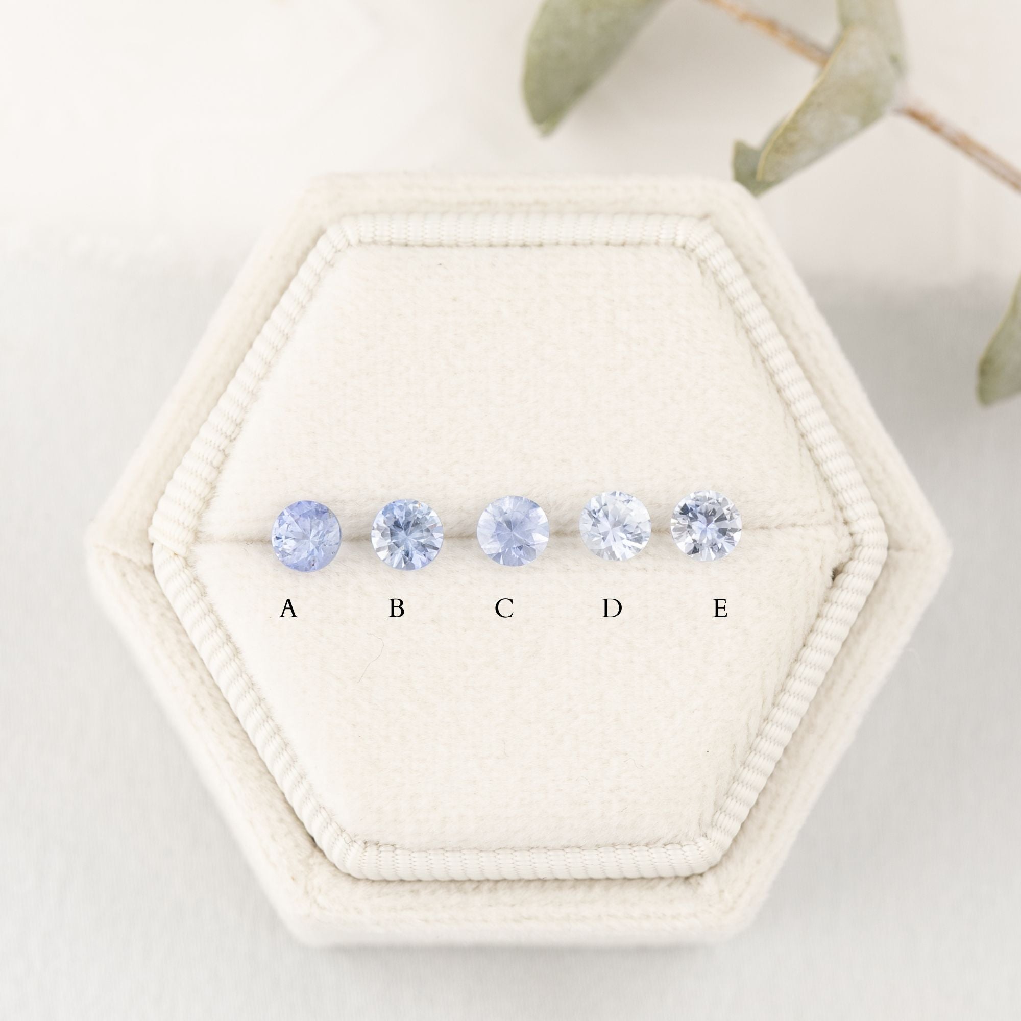 A series of round blue sapphires, set in a row, displayed in a hexagonal white box with each labeled A to E.