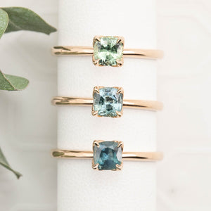 Three rose gold rings with square green gemstones on a white surface.