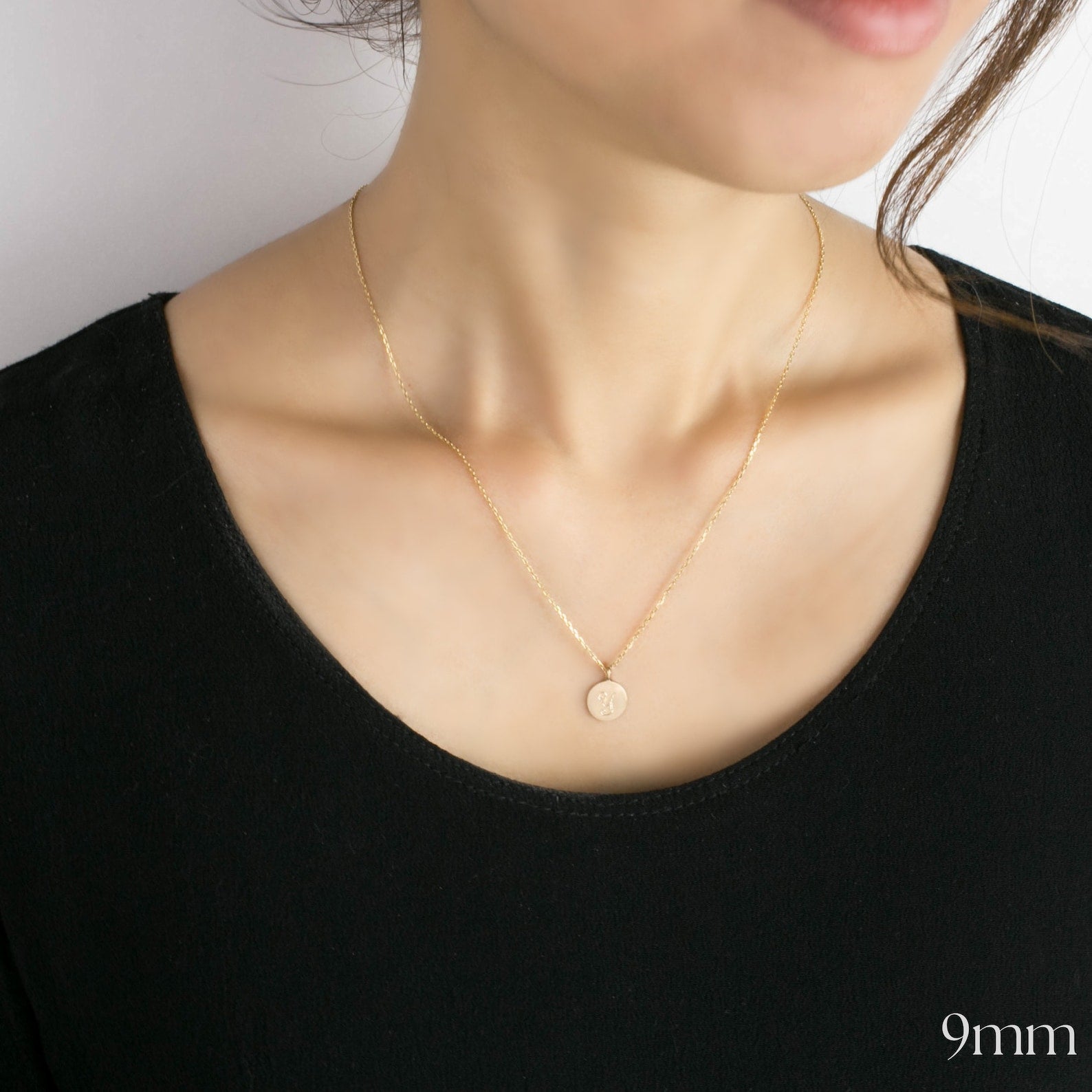 Gold necklace with a small pendant on a person wearing a black top.