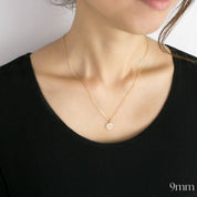 Gold necklace with a small pendant on a person wearing a black top.
