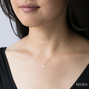 Close-up of a person wearing a delicate gold necklace with a small round pendant on a plain background.