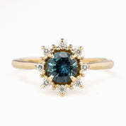 A round-cut blue gemstone ring with accent diamonds arranged in a halo pattern around the center stone, set in a gold band.