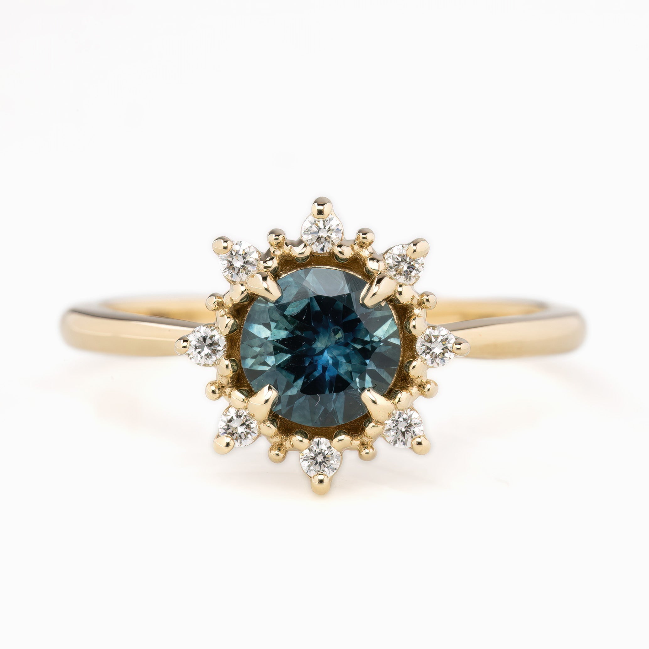 A round-cut blue gemstone ring with accent diamonds arranged in a halo pattern around the center stone, set in a gold band.