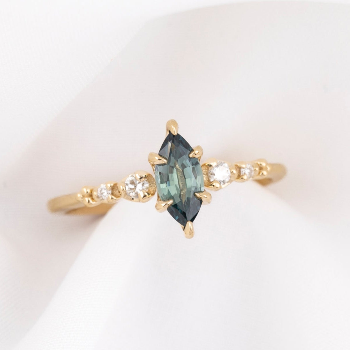 Gold ring with a teal blue marquise sapphire and natural diamonds on a white background