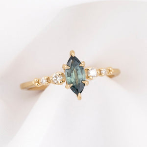 Gold ring with a teal blue marquise sapphire and natural diamonds on a white background