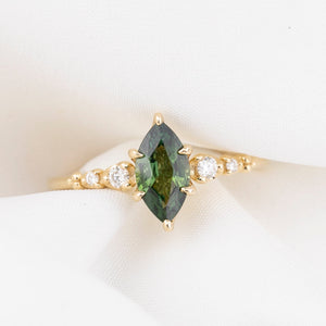 Gold ring with a green marquise sapphire and smaller diamonds on a white background