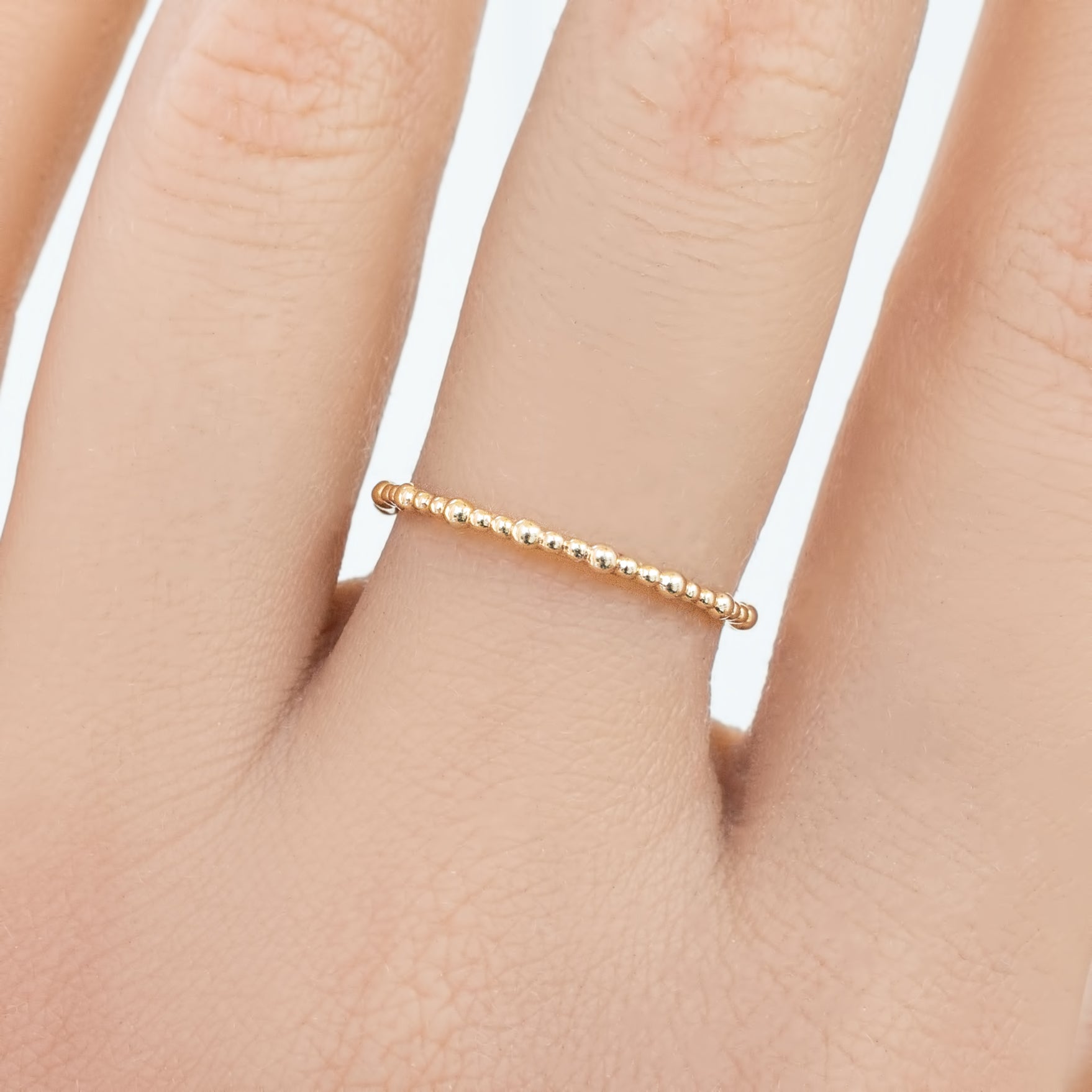 Close-up of a hand wearing a delicate full eternity style gold bead ring with a 1.5mm band width.