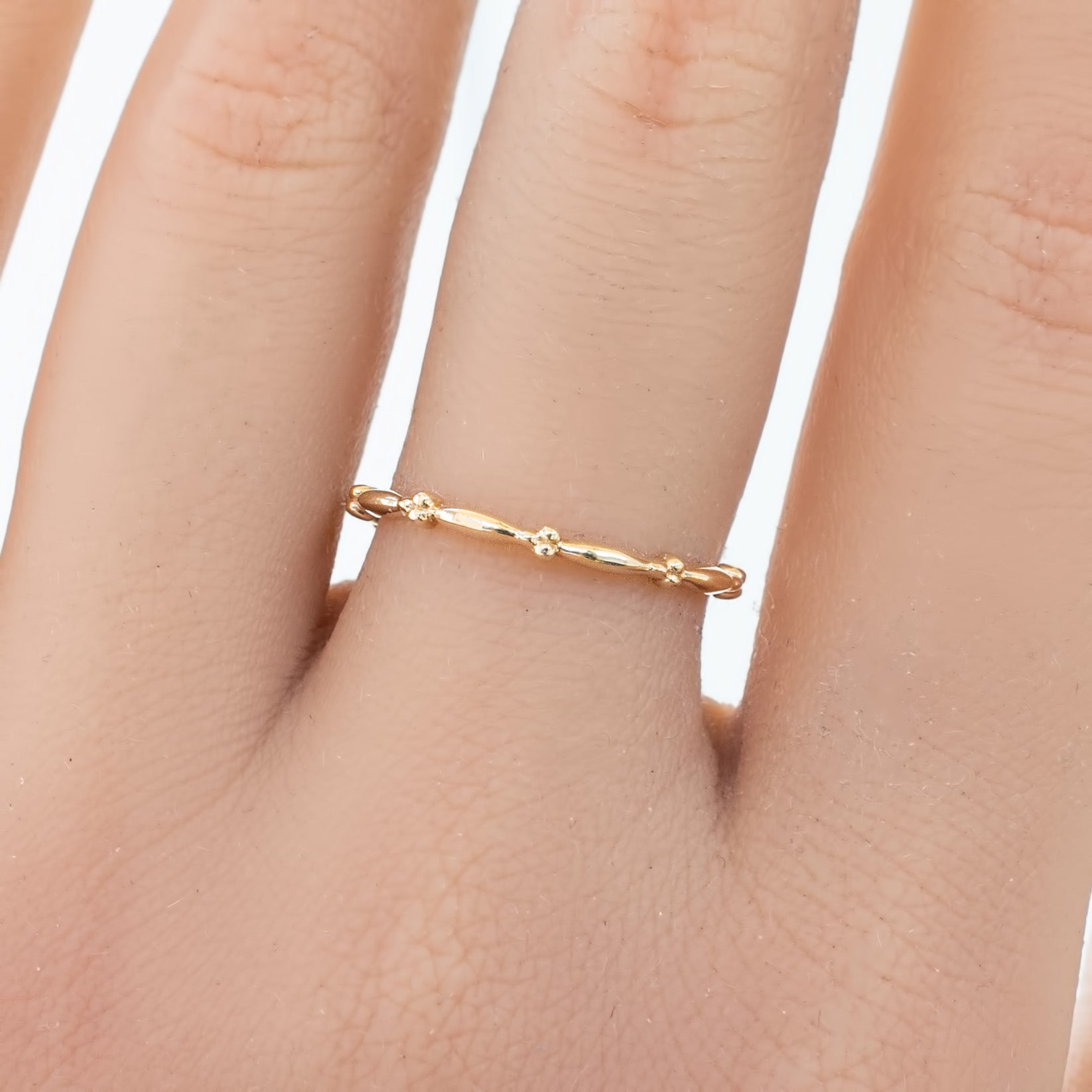 Close-up of a delicate 1.7mm Julia Ring in solid gold with a beaded eternity design worn on a finger