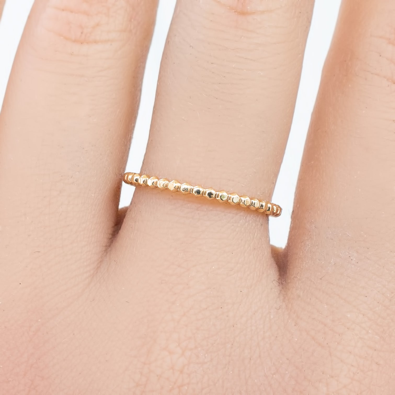 Close-up of a hand wearing a solid gold bead eternity ring with a 1.5mm band width on a finger