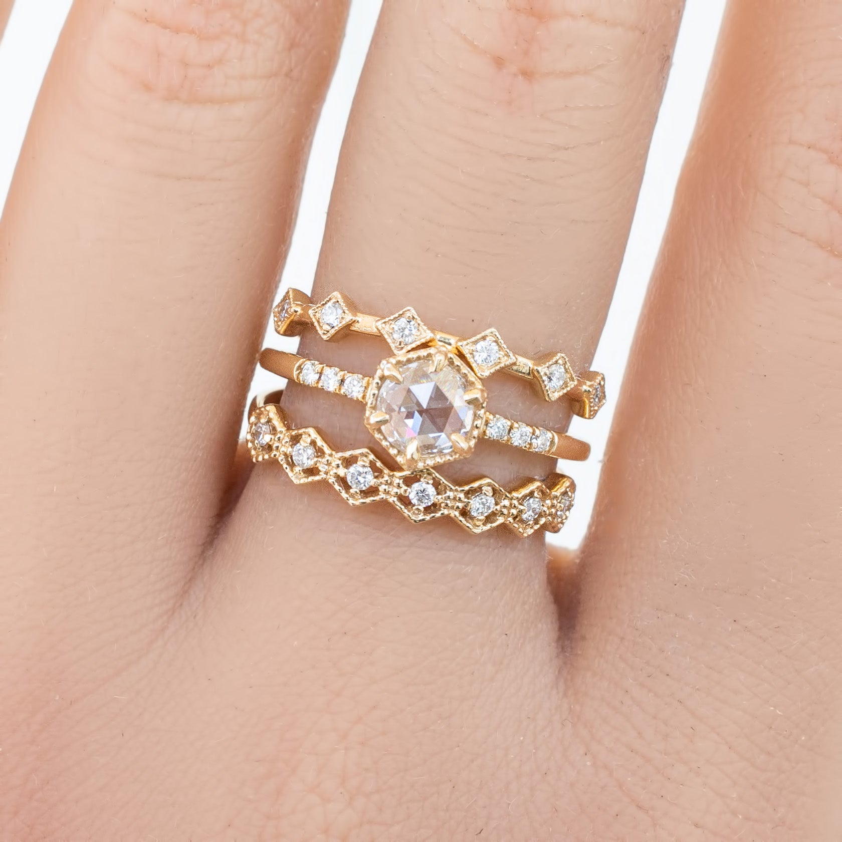 Hand wearing three ethically sourced solid gold rings with natural white diamonds and genuine gemstones