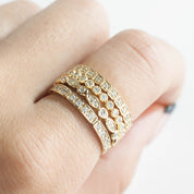 Close-up of a hand wearing four stacked Seren Rings with natural white diamonds in solid gold bands