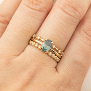 Close-up of a hand wearing three gold rings, including a sapphire solitaire and diamond eternity bands.