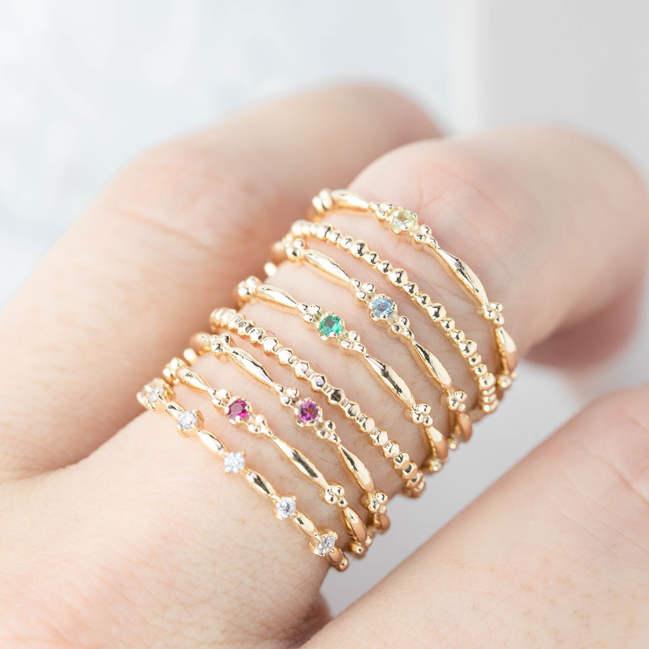 Close-up of a hand wearing multiple delicate gold Distant Star Rings with natural white diamonds and colored gemstones
