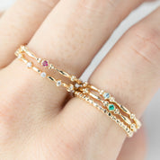 Close-up of a hand wearing delicate 14k gold birthstone rings with various gemstones and textured band designs