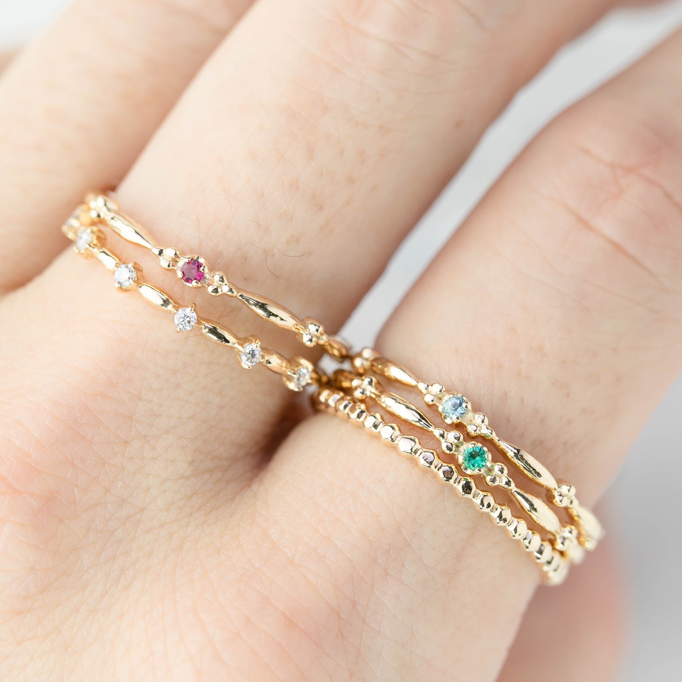 Close-up of a hand wearing delicate 14k gold birthstone rings with various gemstones and textured band designs