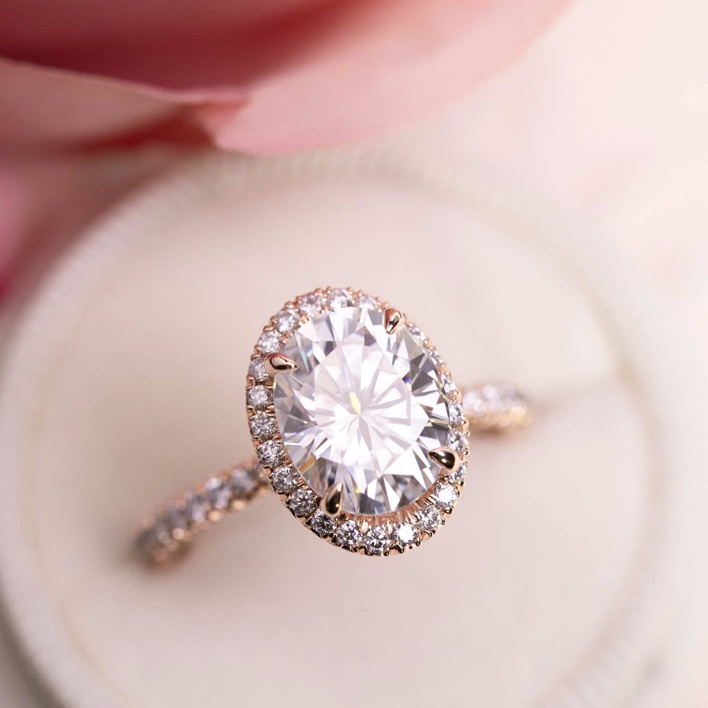 Close-up of a 3ct Neo Moissanite halo ring with French cut down setting on a soft pink background