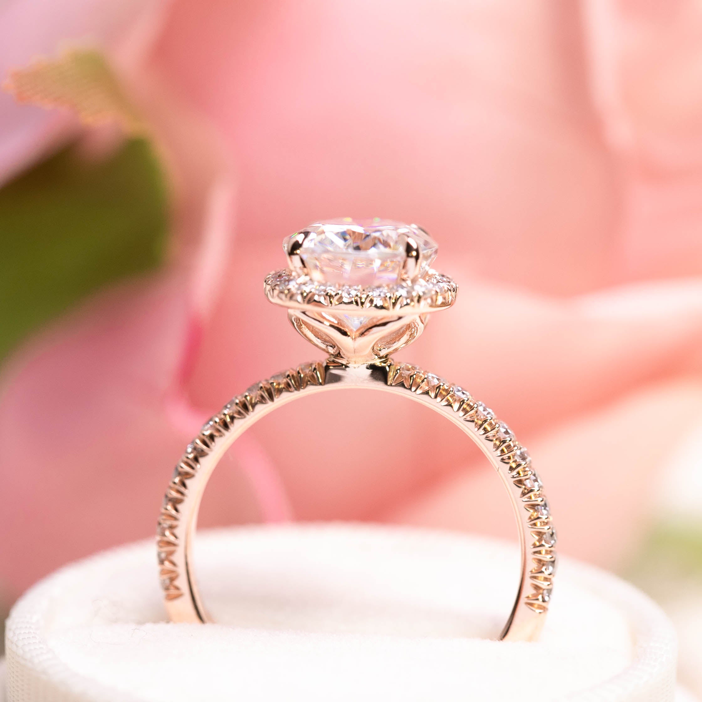3ct Neo Moissanite halo ring with half-eternity diamond band and unique flower-shaped base craftsmanship on pink background.