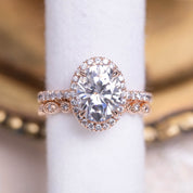 Rose gold Neo Moissanite halo ring with 3ct oval center stone and diamond accented half-eternity band.