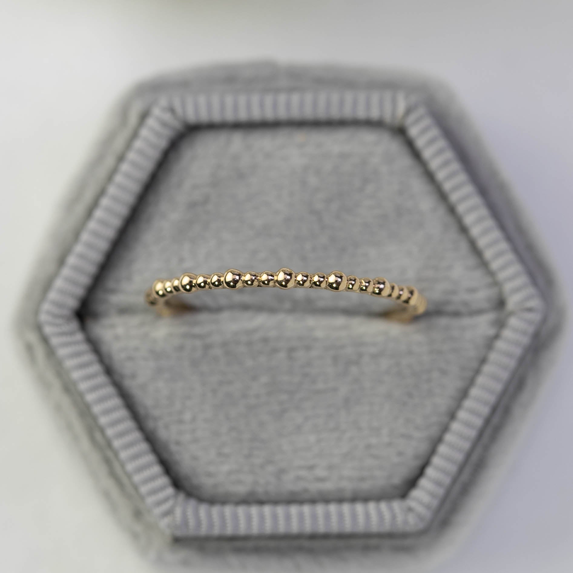 Gold full eternity bead ring displayed in a gray hexagonal recyclable kraft ring box, band width approx. 1.5mm