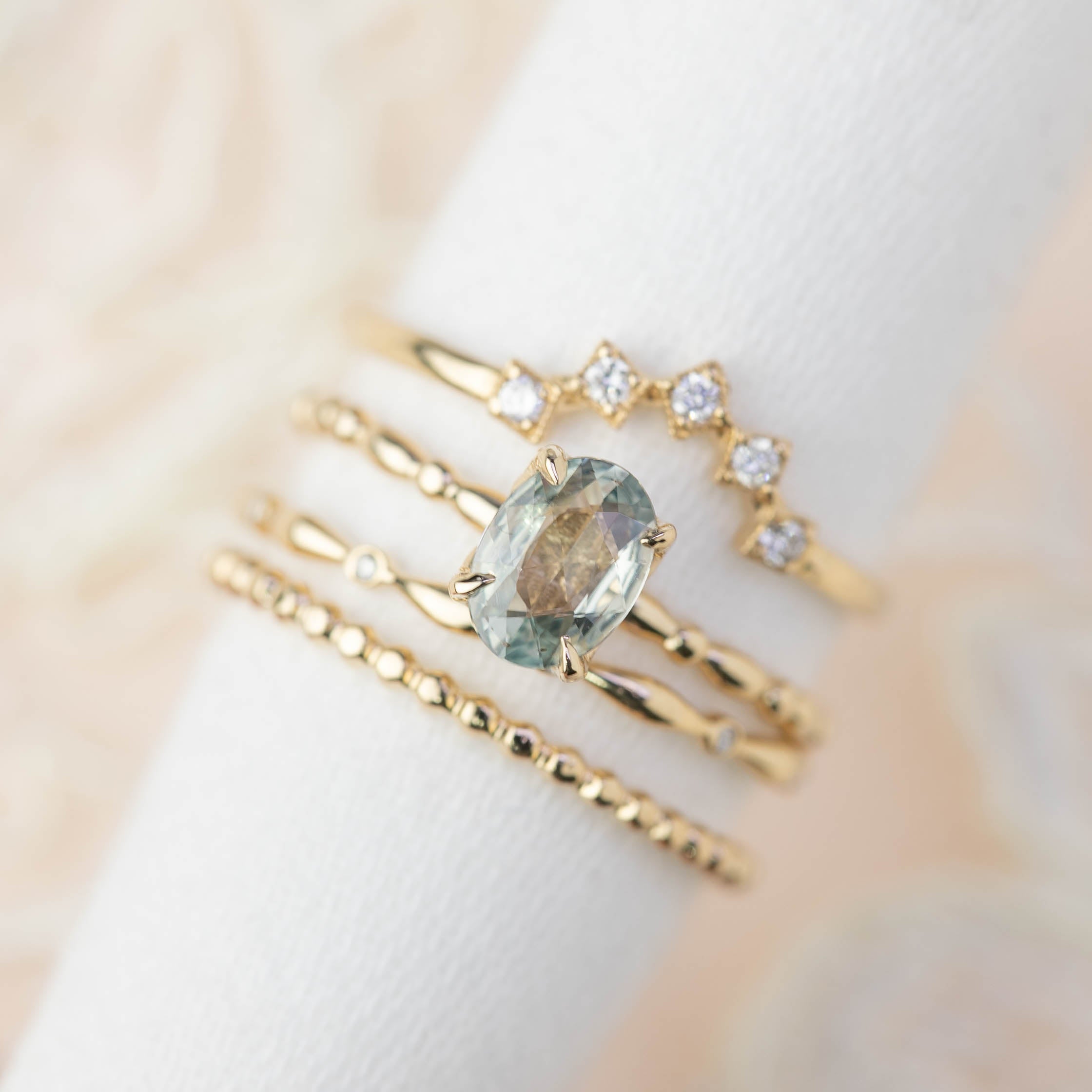 Stack of delicate gold rings featuring a natural diamond eternity band and a central oval gemstone ring