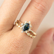 Close-up of a hand wearing a gold ring with a dark blue center stone surrounded by small diamonds