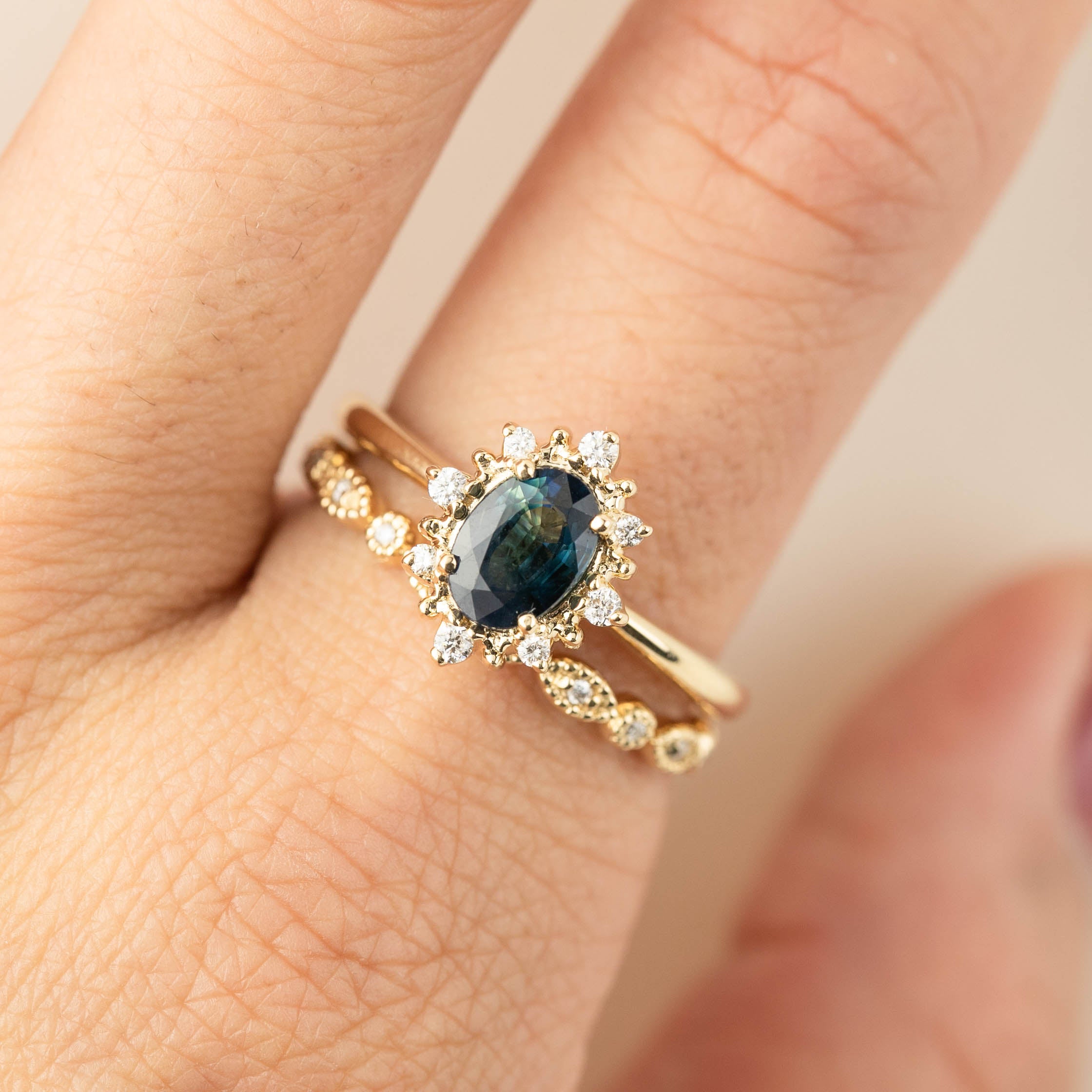 Close-up of a hand wearing a gold ring with a dark blue center stone surrounded by small diamonds