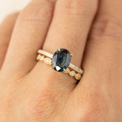 Close-up of hand wearing a gold ring with an oval dark gemstone and two diamond-studded bands stacked together