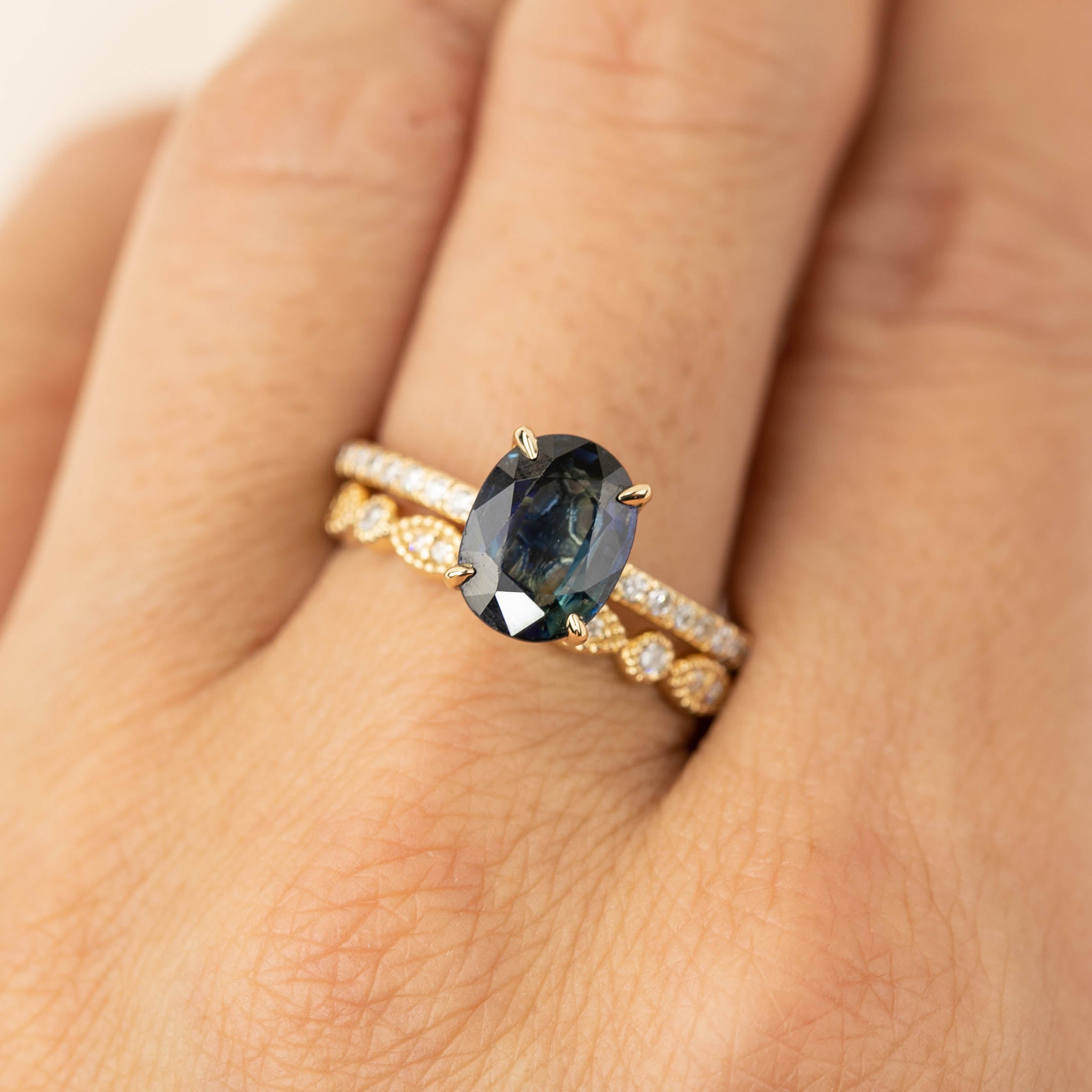 Close-up of hand wearing a gold ring with an oval dark gemstone and two diamond-studded bands stacked together