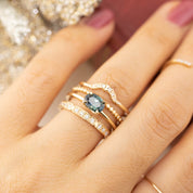 Close-up of hand wearing layered gold rings including a dark emerald-cut stone and diamond accents on thin bands