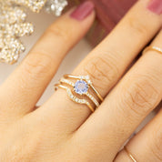 Close-up of a hand wearing Isabel's Curved Ring with natural white diamonds and a blue gemstone on a gold band