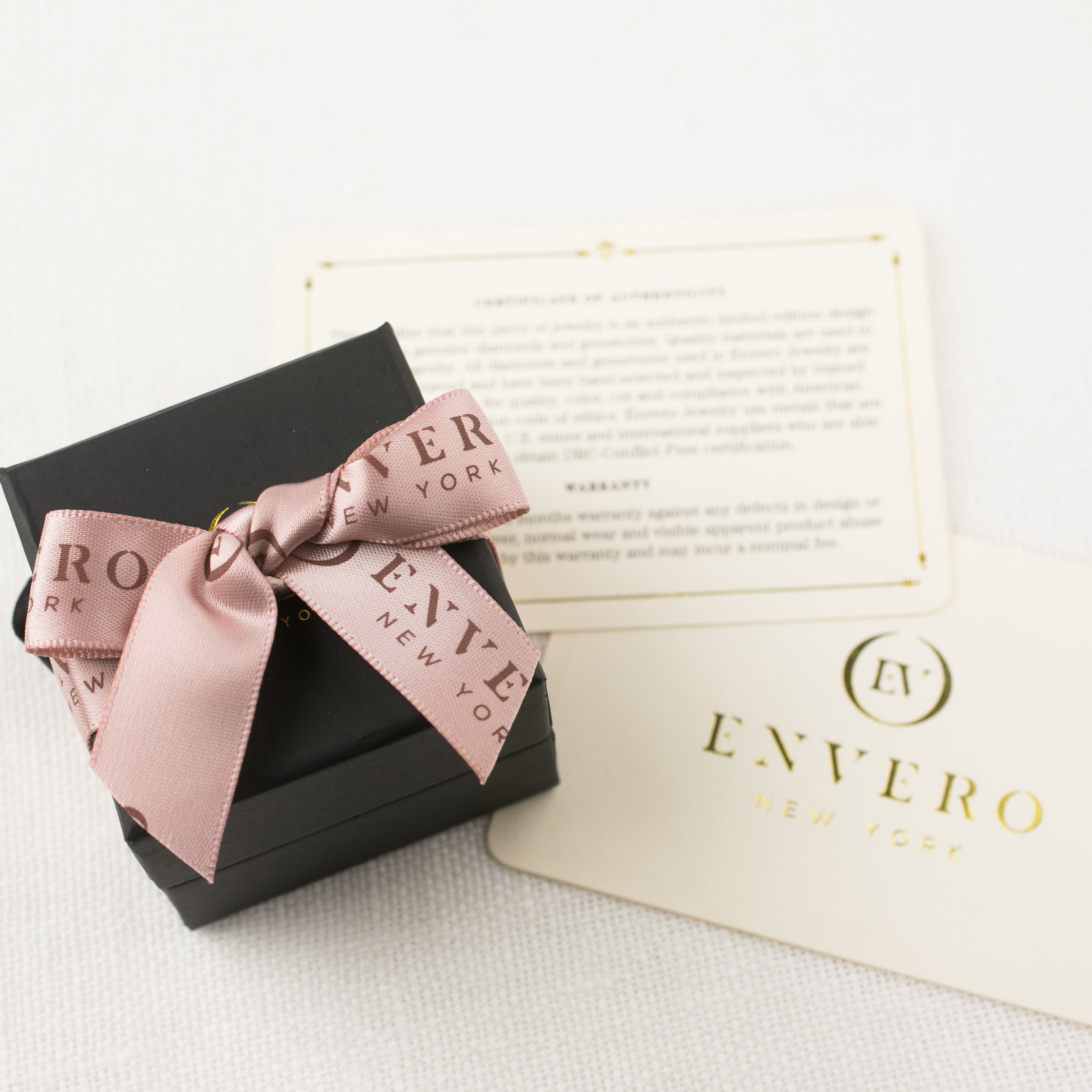 Black Envero gift box with pink bow and two gold-stamped cards on white textured surface