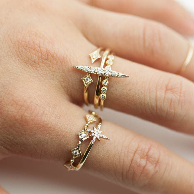 Close-up of a hand wearing two 14k gold Starburst Diamond Rings with brilliant cut white diamonds sparkling.