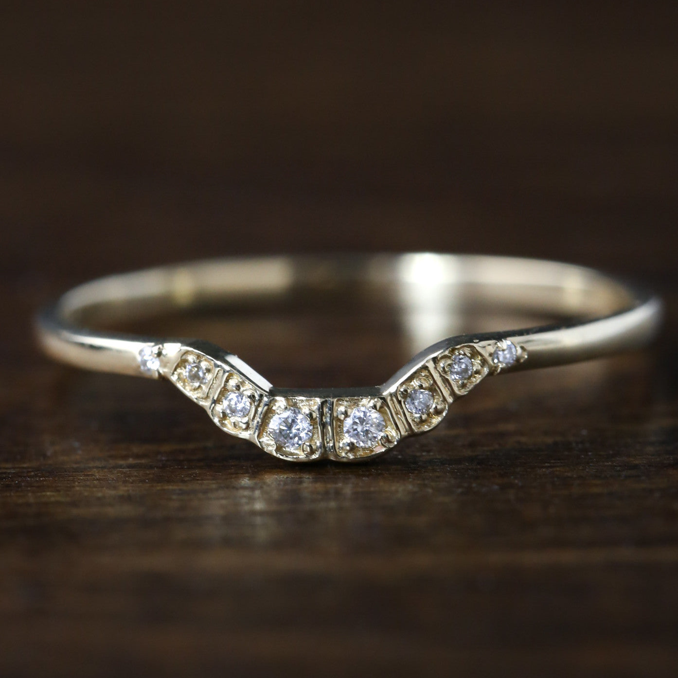 Solid gold curved ring with natural white diamonds set in a U-shaped design on a wooden surface.