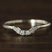 Solid gold curved ring with natural white diamonds set in a U-shaped design on a wooden surface.