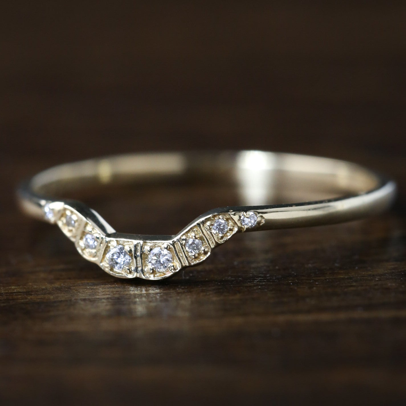 Ethically sourced solid gold curved ring with natural white diamonds in a U-shape design on wooden surface.