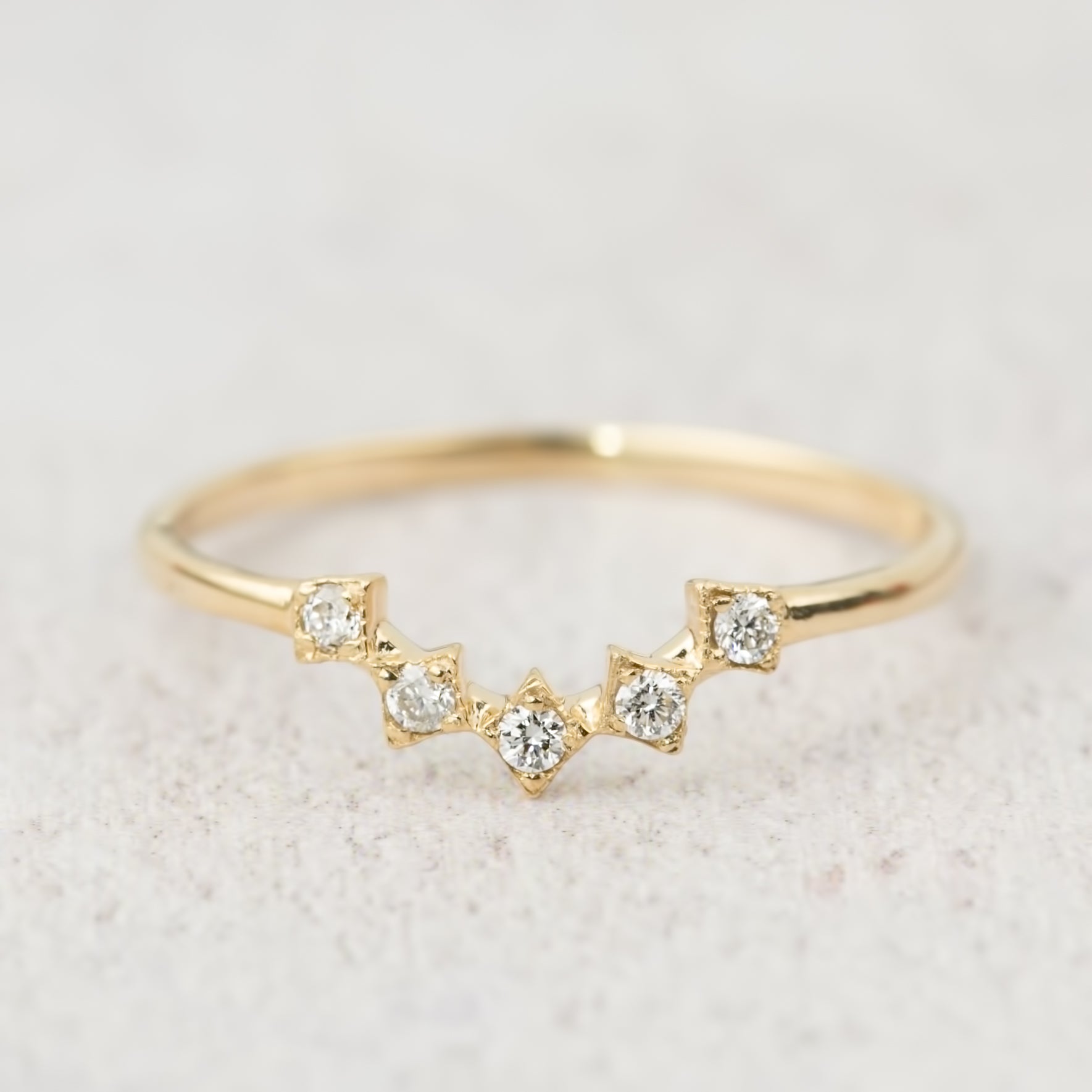 Delicate gold star tiara ring with five natural white diamonds set in a curved V-shaped band on neutral background