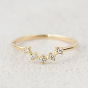 Delicate gold star tiara ring with five natural white diamonds set in a curved V-shaped band on neutral background