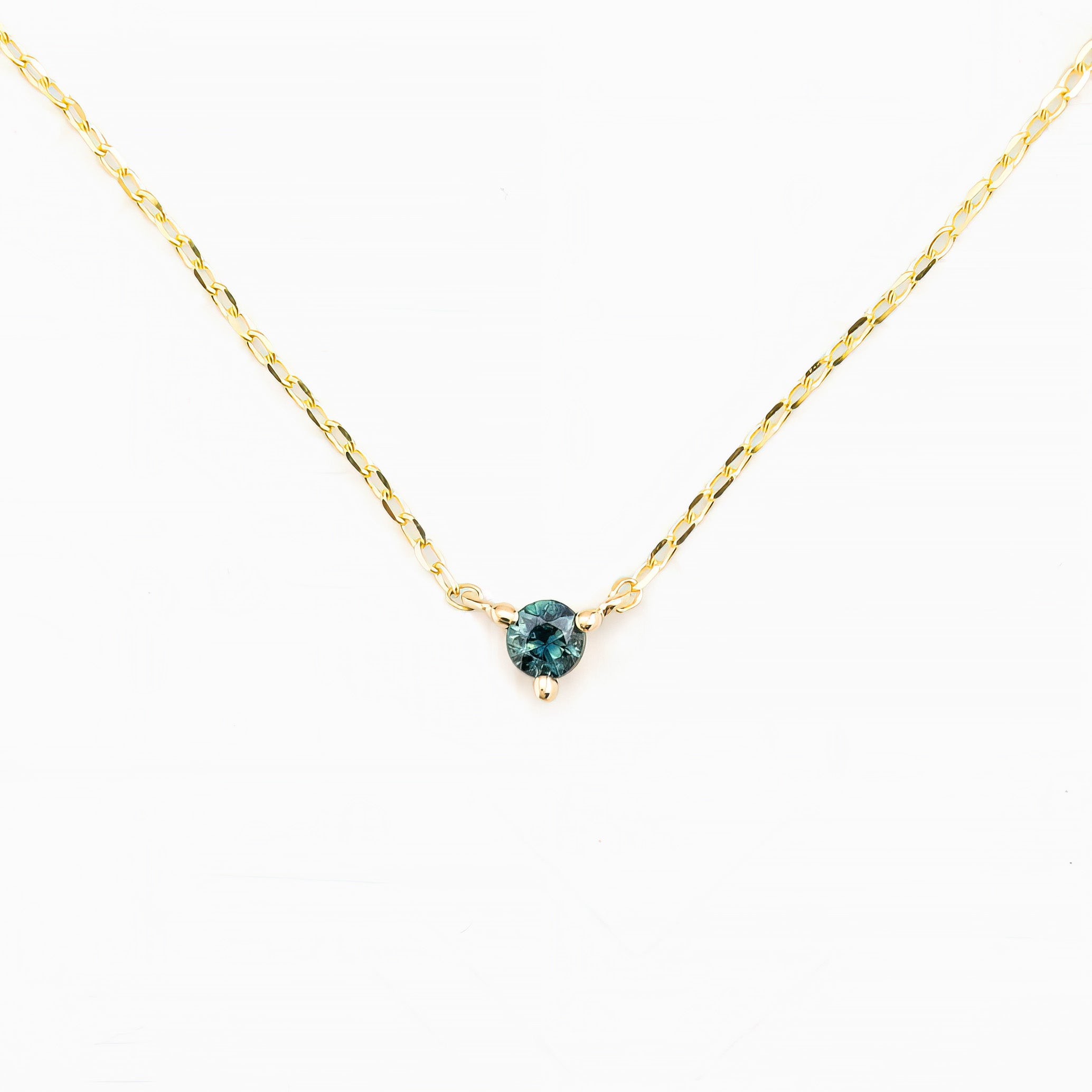 A gold-colored necklace with a round 3-4mm blue gemstone set in a three-prong setting with a spring ring clasp closure.