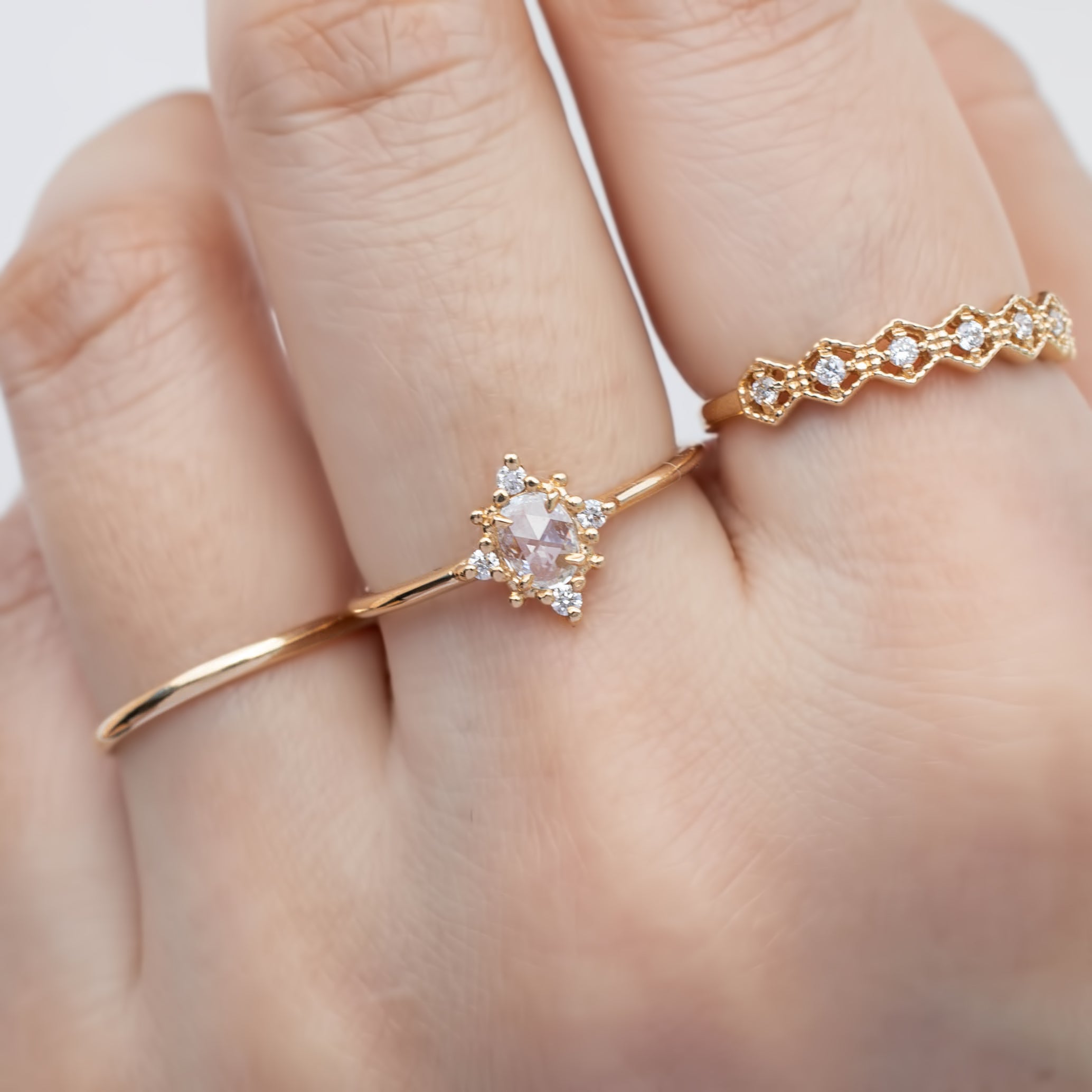 Close-up of a hand wearing a delicate gold Victoria Ring with a 0.41ct oval rose cut diamond and white accent diamonds