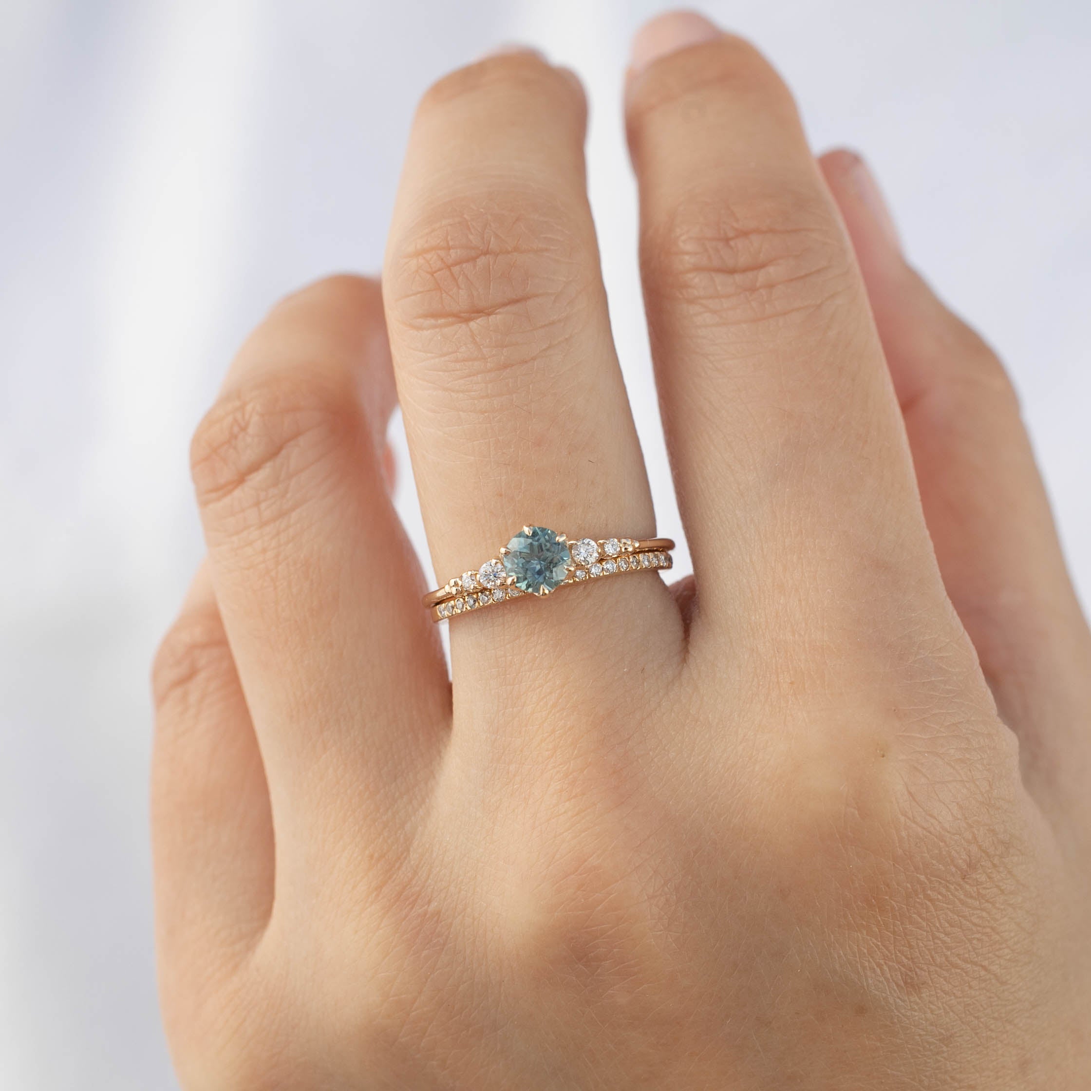 Hand wearing a slim 1.3mm gold diamond band with natural white diamonds on ring finger against a light background